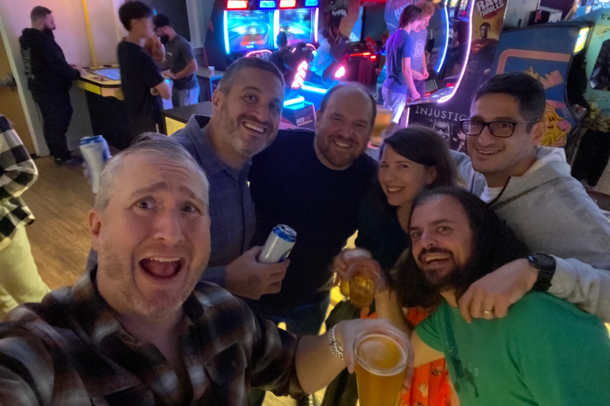 Six friends crowded into one selfie, beers up, at the after-party